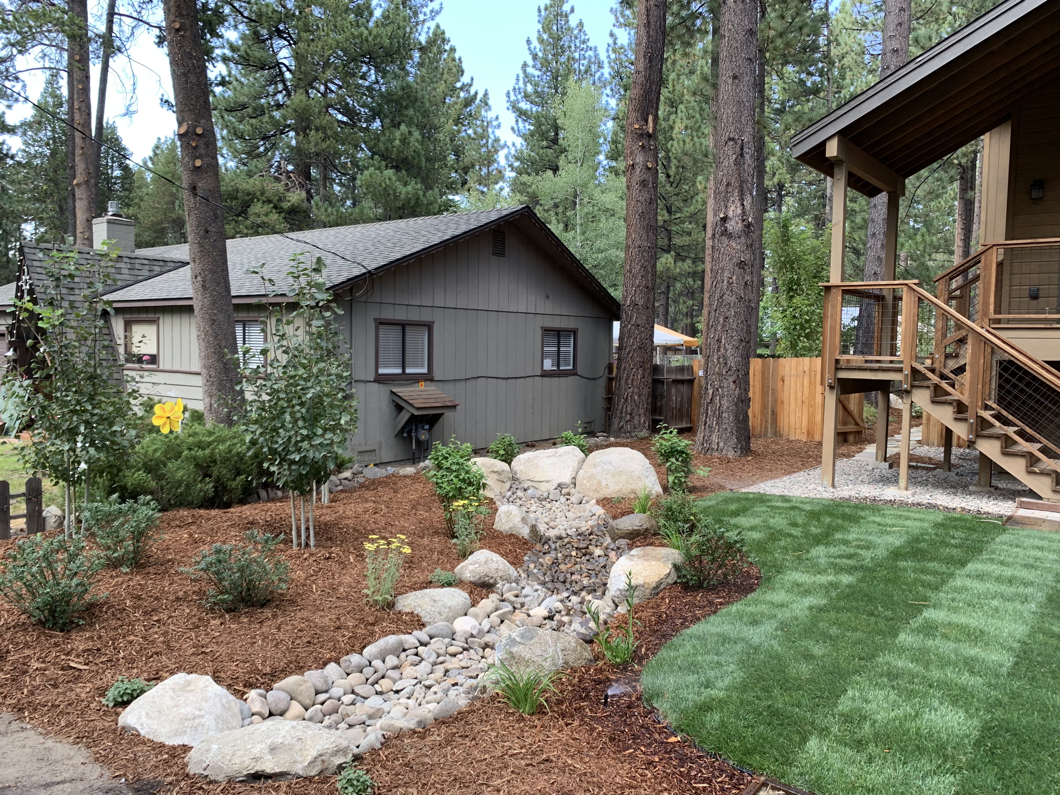 Dry creek drainage, river rock, mulch beds, boulders, and clean lawn edge at a Tahoe property