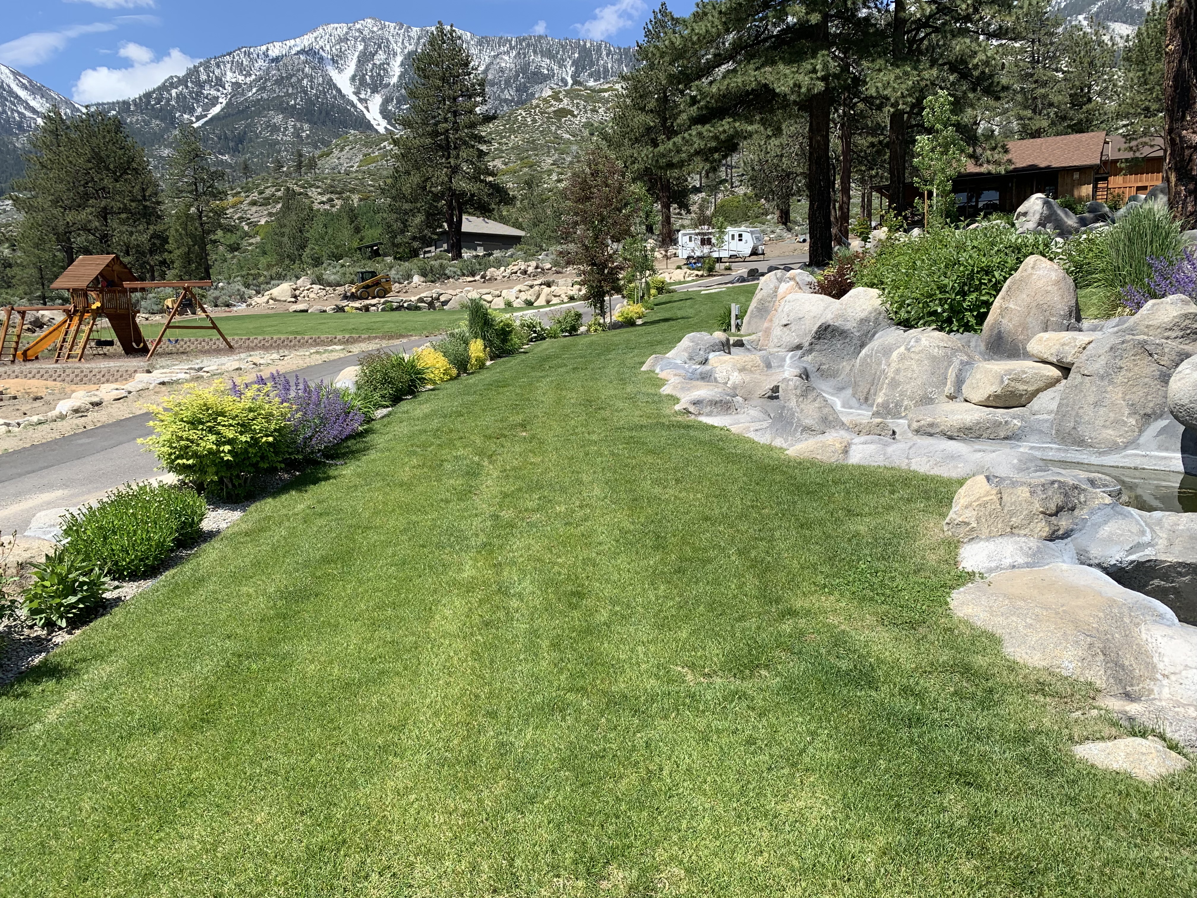 Lush irrigated Tahoe lawn with colorful plantings, granite boulders, and mountain backdrop