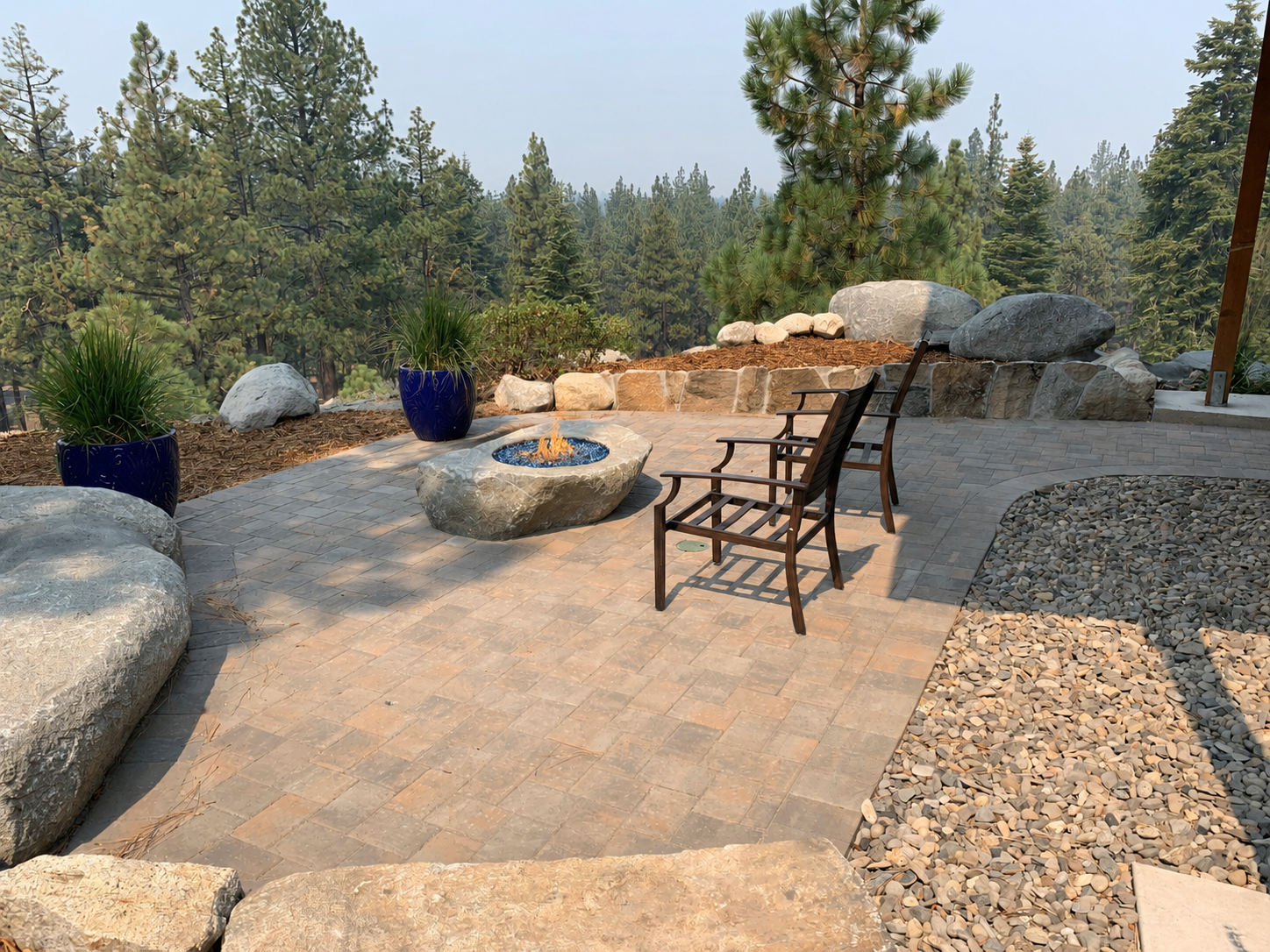 Paver patio with boulder fire feature, seating, retaining wall, granite boulders, and Tahoe pine backdrop